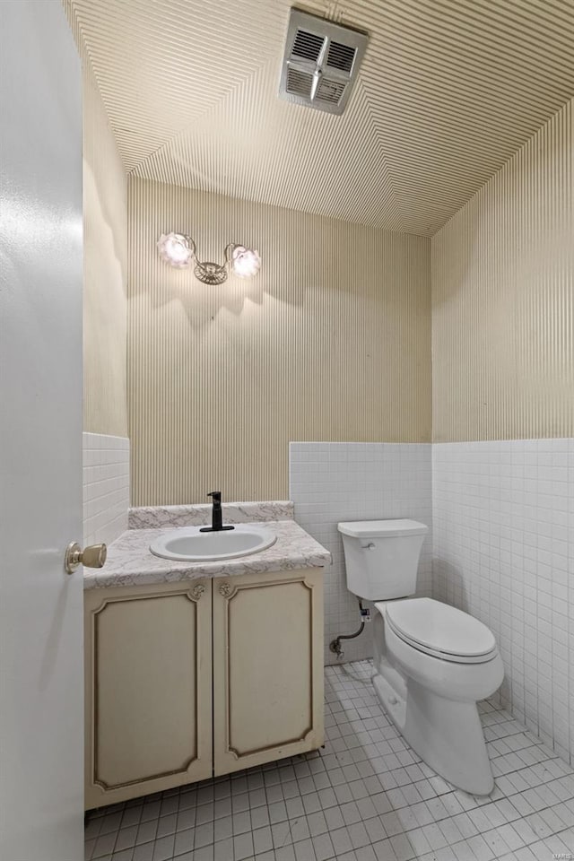 half bathroom with visible vents, toilet, tile walls, vanity, and tile patterned flooring