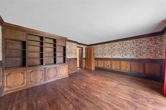 unfurnished living room featuring ornamental molding, wallpapered walls, wainscoting, and dark wood-type flooring
