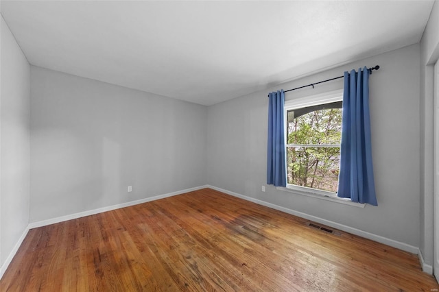 empty room with baseboards, visible vents, and wood finished floors