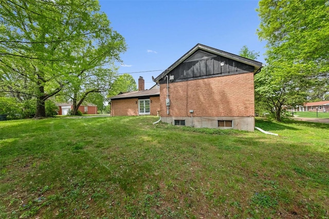 back of property featuring a lawn, a chimney, french doors, and brick siding