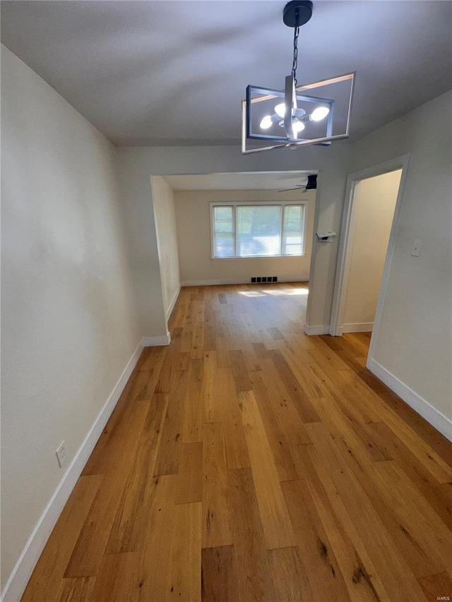 unfurnished dining area featuring light wood-type flooring, visible vents, an inviting chandelier, and baseboards