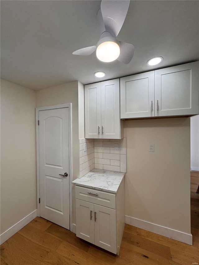 kitchen with white cabinetry, baseboards, light wood-type flooring, a ceiling fan, and backsplash