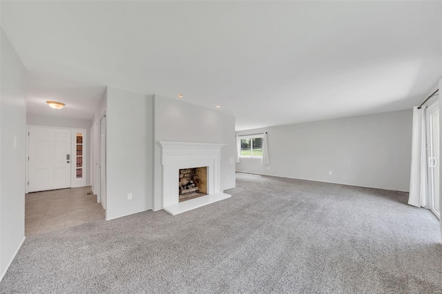 unfurnished living room with a fireplace with raised hearth, tile patterned floors, and carpet