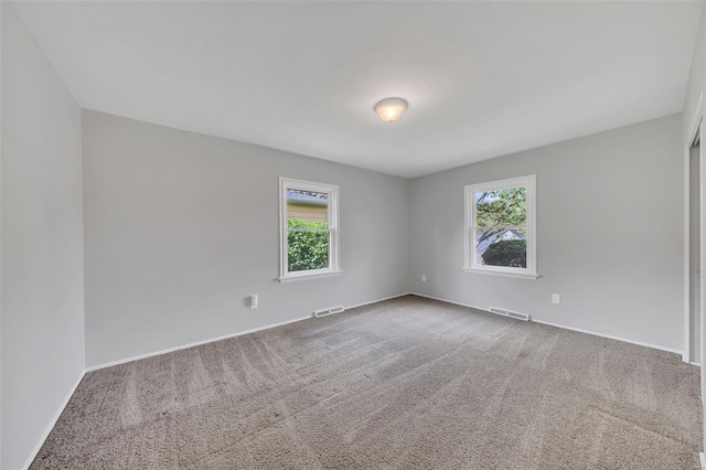 unfurnished room featuring visible vents, a wealth of natural light, and carpet flooring