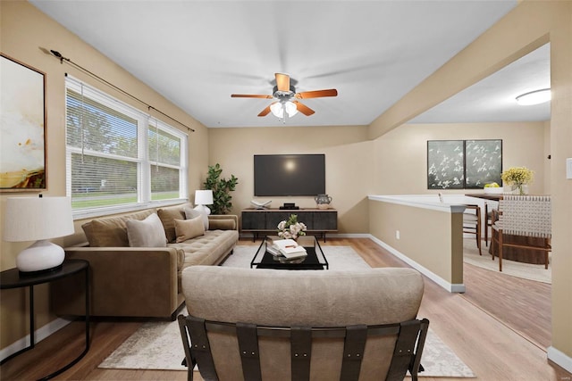 living room with light wood-style floors, baseboards, and ceiling fan