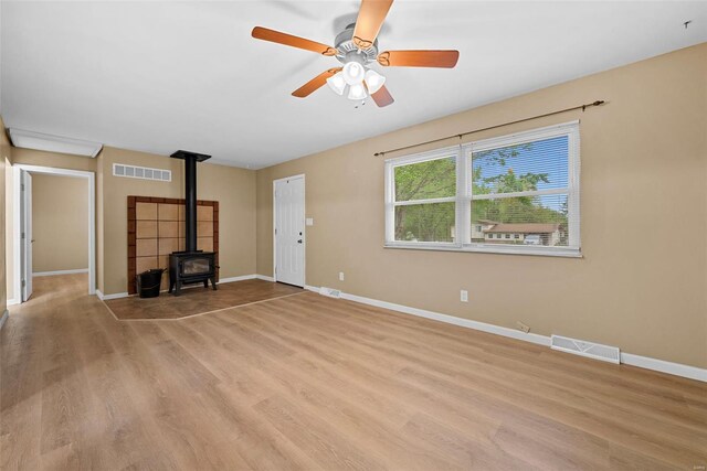 unfurnished living room with a ceiling fan, visible vents, wood finished floors, and a wood stove