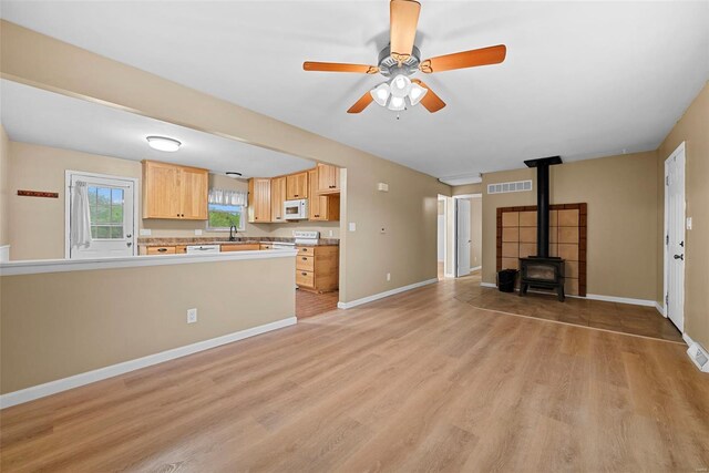 unfurnished living room with visible vents, a wood stove, light wood-style floors, ceiling fan, and a sink