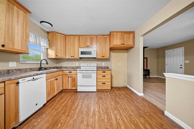 kitchen with light brown cabinetry, white appliances, baseboards, a sink, and light wood finished floors