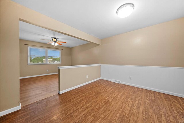 empty room with a ceiling fan, visible vents, wood finished floors, baseboards, and beamed ceiling