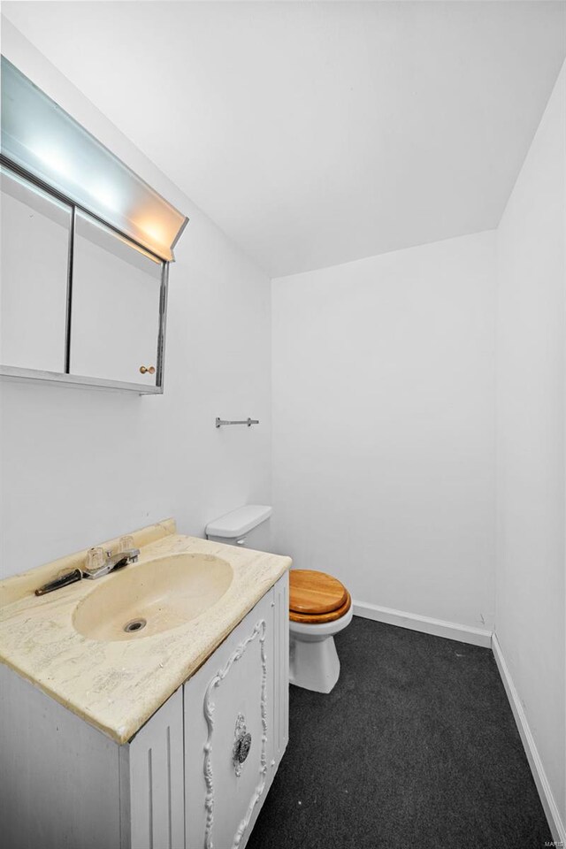 half bath with vanity, baseboards, and toilet