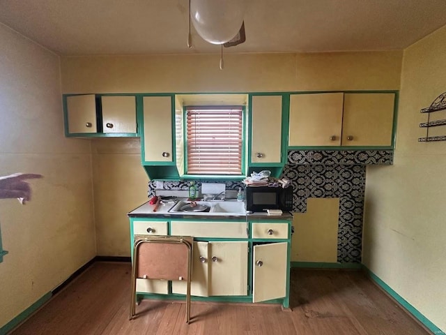 kitchen featuring light wood finished floors, black microwave, a sink, and baseboards