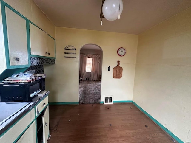 interior space featuring black microwave, wood finished floors, visible vents, and arched walkways