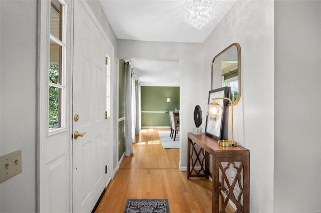 hall with baseboards, light wood-style flooring, and a notable chandelier