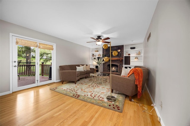 living area with ceiling fan, visible vents, a brick fireplace, wood finished floors, and baseboards