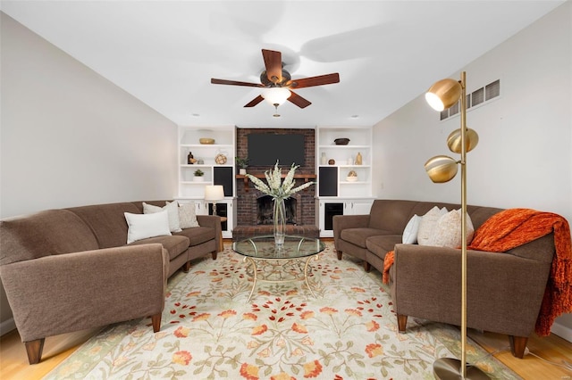 living room featuring ceiling fan, visible vents, built in features, a fireplace, and light wood-type flooring