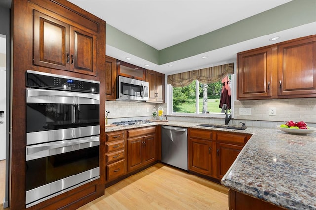 kitchen with light stone counters, a sink, light wood-style flooring, appliances with stainless steel finishes, and backsplash