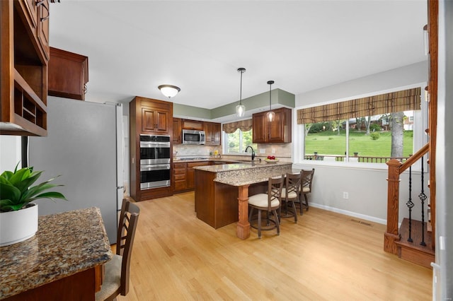 kitchen with a kitchen breakfast bar, light wood-type flooring, tasteful backsplash, a sink, and appliances with stainless steel finishes
