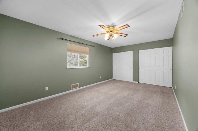 unfurnished bedroom with carpet, two closets, a ceiling fan, baseboards, and visible vents