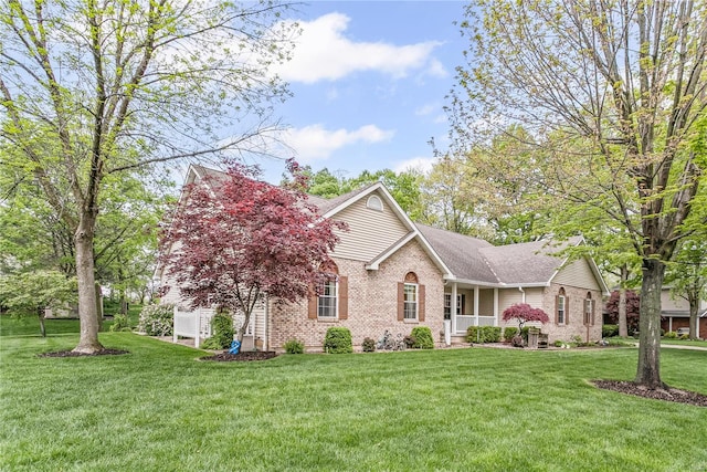 view of front of house with a shingled roof, brick siding, covered porch, and a front lawn