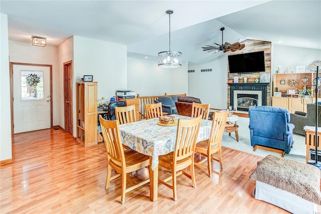 dining area with light wood finished floors, a fireplace, visible vents, lofted ceiling, and ceiling fan with notable chandelier