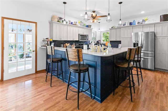 kitchen with stainless steel appliances, ceiling fan, light wood-style floors, and backsplash