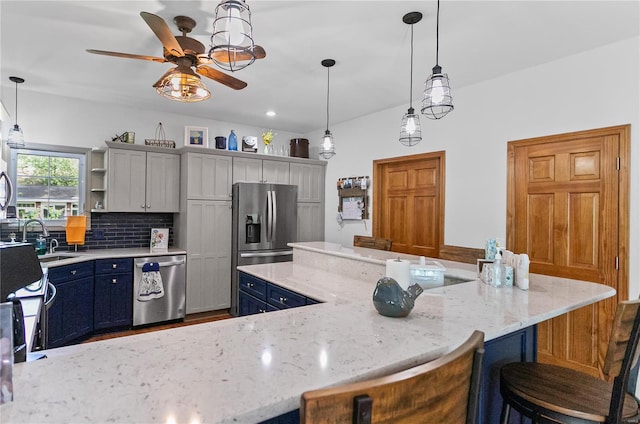 kitchen featuring a sink, stainless steel appliances, a kitchen bar, a ceiling fan, and backsplash