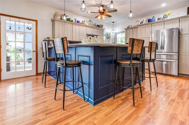 kitchen with a breakfast bar, ceiling fan, stainless steel refrigerator with ice dispenser, and light wood-style floors
