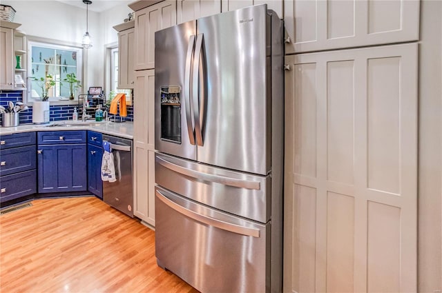 kitchen featuring blue cabinetry, stainless steel appliances, light countertops, a sink, and light wood-type flooring