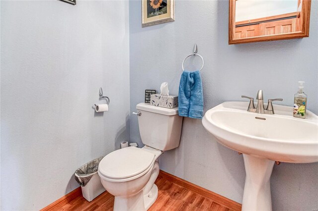 half bathroom with baseboards, wood finished floors, toilet, and a sink