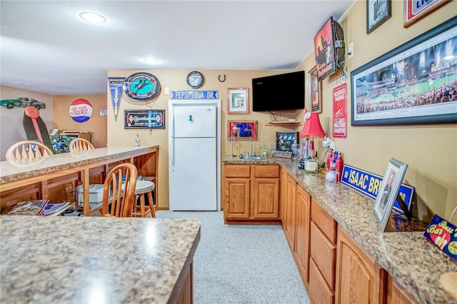 kitchen featuring brown cabinetry, recessed lighting, light colored carpet, and freestanding refrigerator