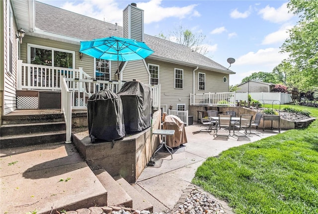 back of house featuring a deck, a chimney, a shingled roof, and a patio area