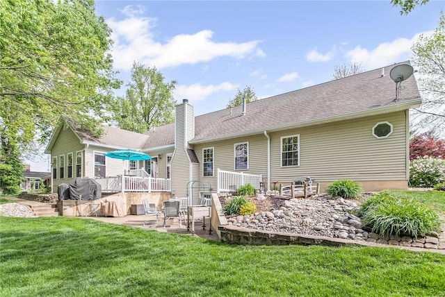back of property featuring a deck, a chimney, a yard, a shingled roof, and a patio area