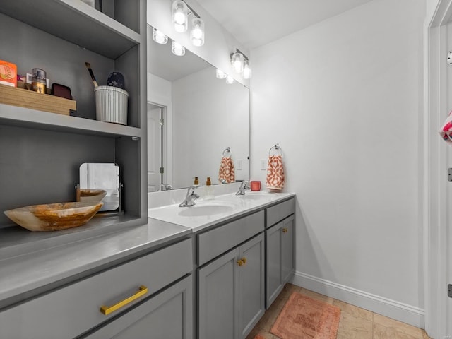 full bath with stone tile floors, double vanity, baseboards, and a sink