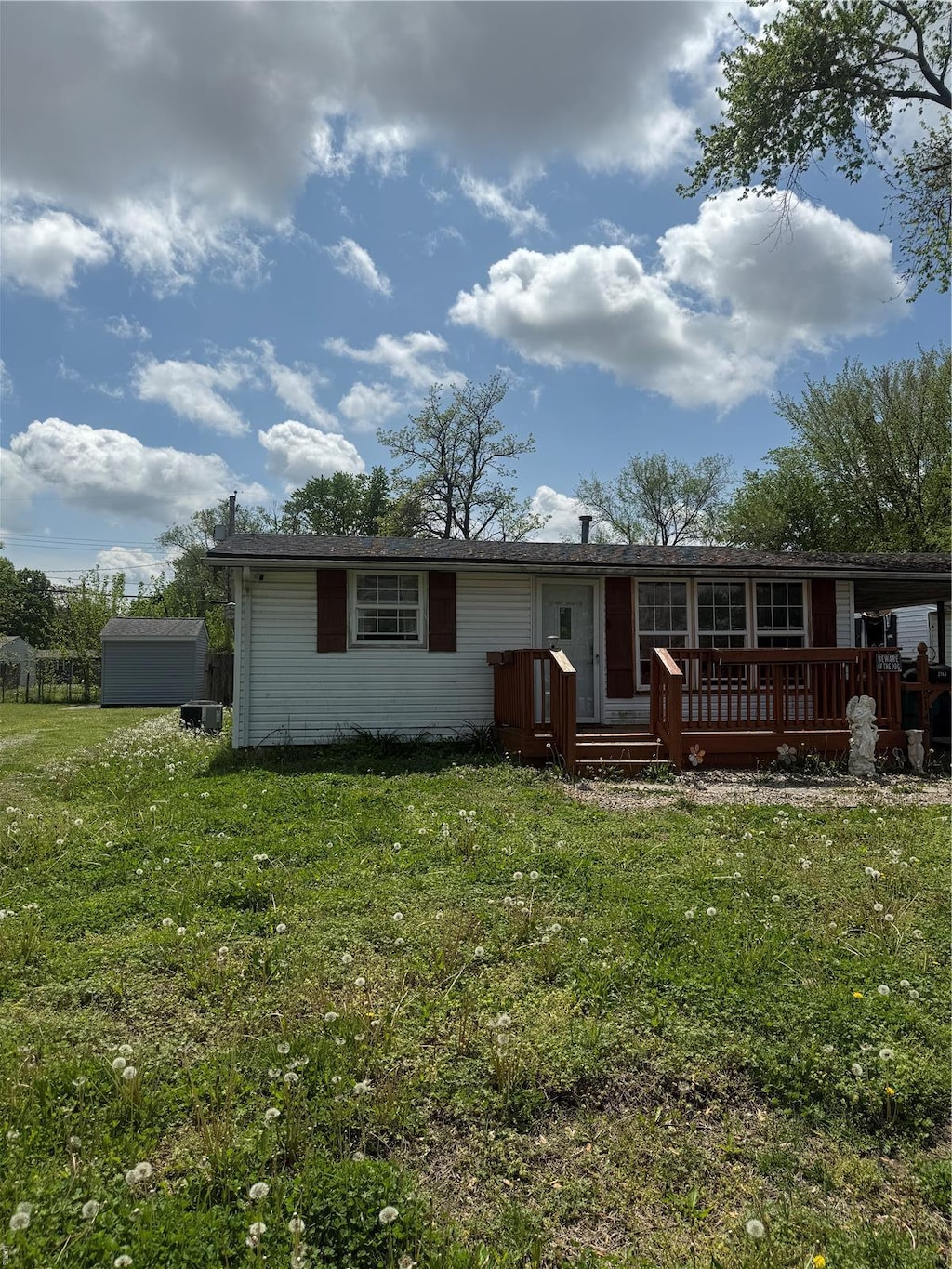 back of house with a storage shed, a yard, a wooden deck, and an outbuilding