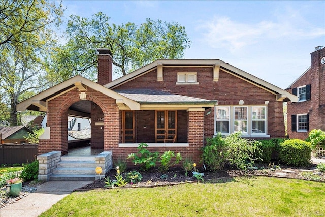 bungalow featuring a chimney, covered porch, fence, brick siding, and a front lawn