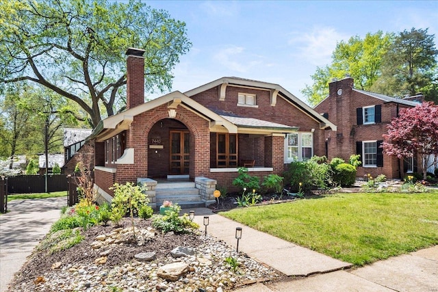 view of front facade featuring a chimney, covered porch, brick siding, fence, and a front yard