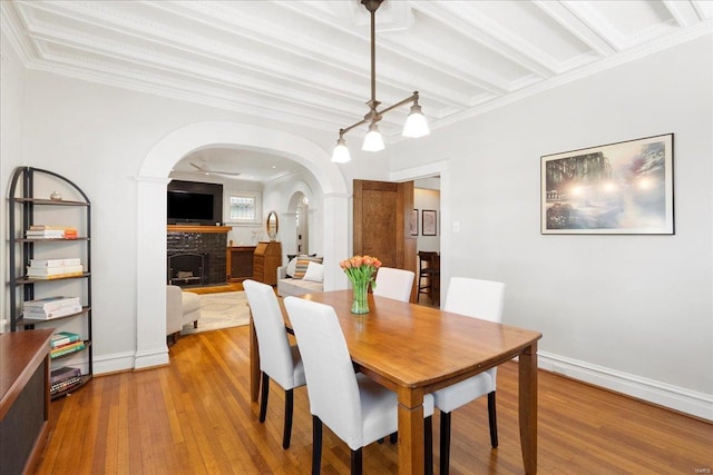 dining space with baseboards, arched walkways, ornamental molding, a fireplace, and wood finished floors