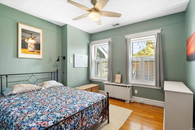 bedroom featuring light wood-style flooring, radiator heating unit, ceiling fan, baseboards, and visible vents