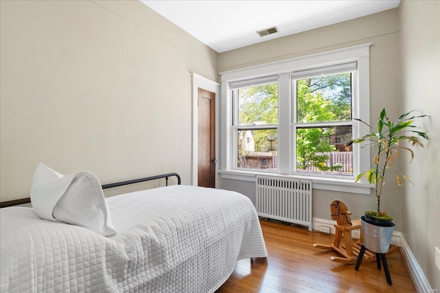 bedroom featuring radiator, visible vents, hardwood / wood-style floors, and baseboards