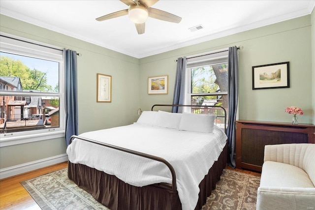 bedroom with a ceiling fan, visible vents, baseboards, ornamental molding, and wood finished floors
