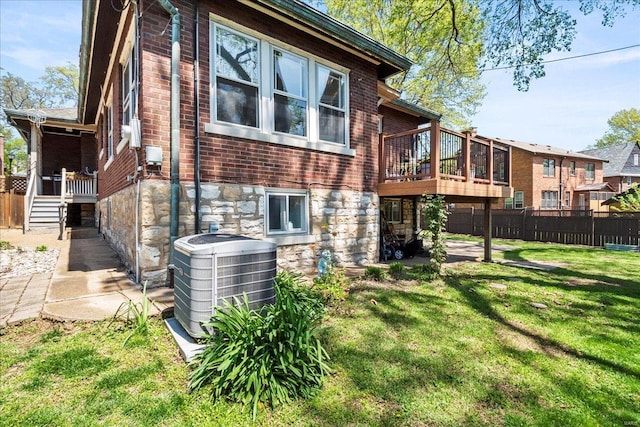 rear view of house featuring brick siding, fence, stone siding, cooling unit, and a lawn