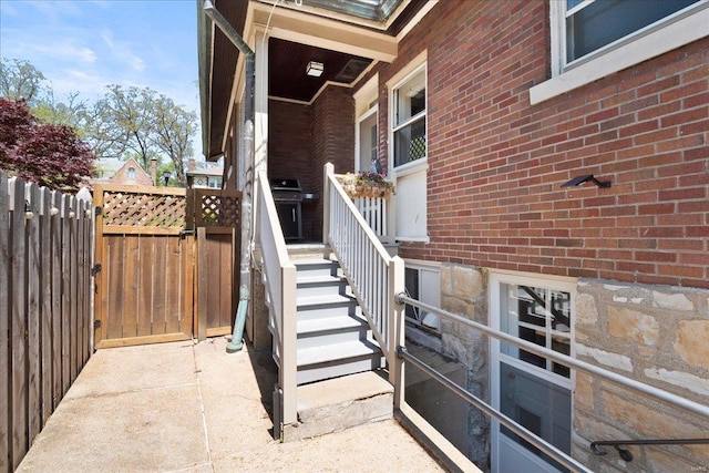 view of exterior entry featuring brick siding and fence