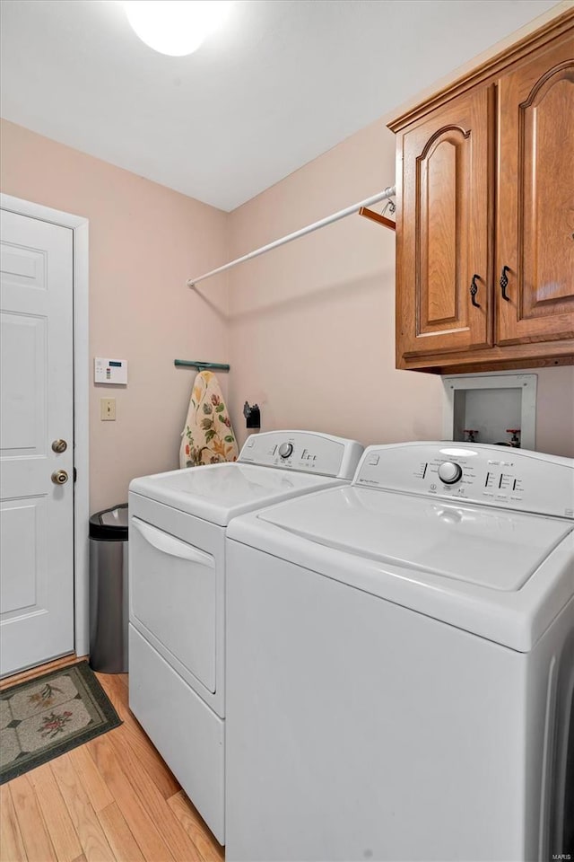 laundry room featuring washing machine and dryer, light wood-type flooring, and cabinet space