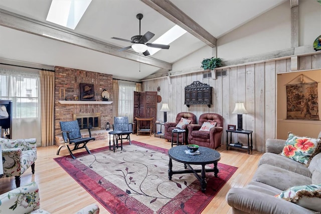 living room featuring ceiling fan, vaulted ceiling with skylight, a fireplace, wood walls, and wood finished floors