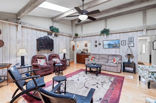 living area featuring wooden walls, ceiling fan, beamed ceiling, and wood finished floors