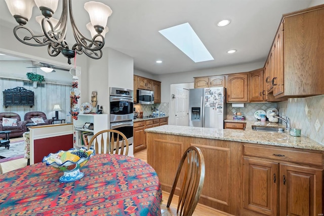 kitchen featuring an inviting chandelier, decorative backsplash, a peninsula, a sink, and stainless steel appliances