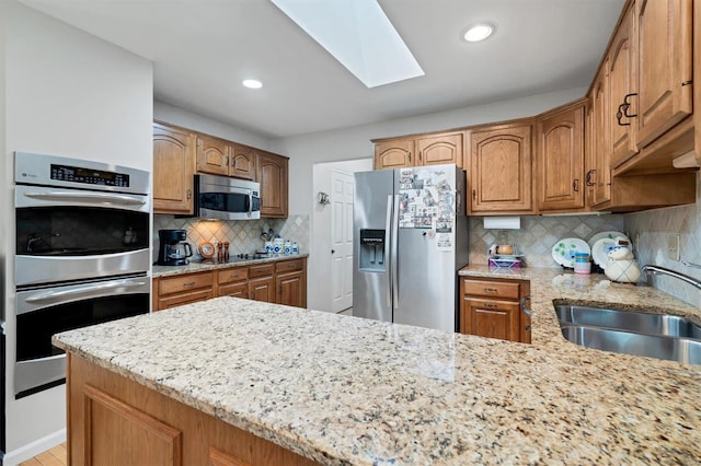 kitchen featuring light stone countertops, tasteful backsplash, a sink, a skylight, and stainless steel appliances