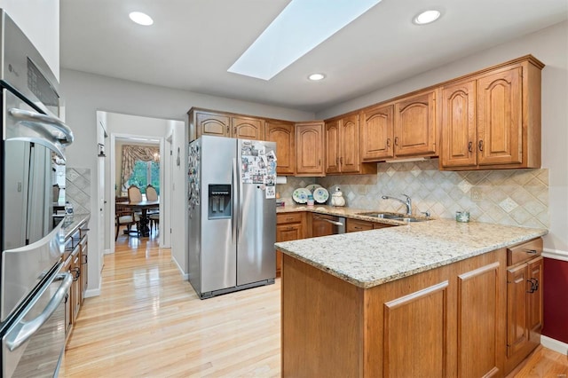 kitchen featuring appliances with stainless steel finishes, light stone counters, a sink, a peninsula, and a skylight