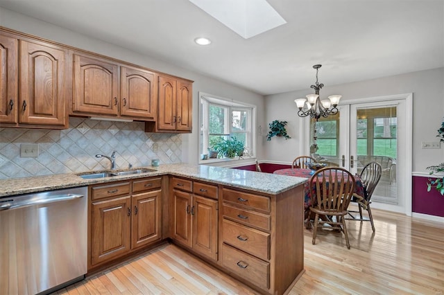 kitchen with stainless steel dishwasher, a peninsula, light stone counters, a sink, and light wood finished floors