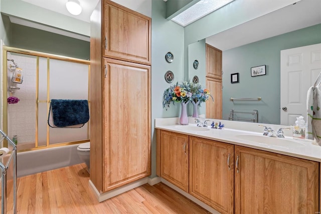 full bathroom with a sink, bath / shower combo with glass door, double vanity, and wood finished floors